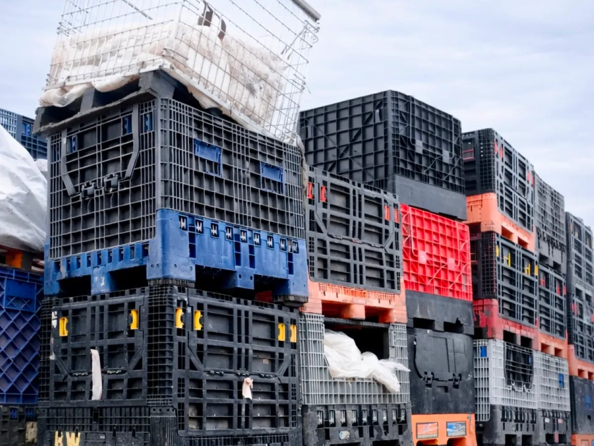 Stacked black, red and blue plastic bulk containers in an outdoor yard
